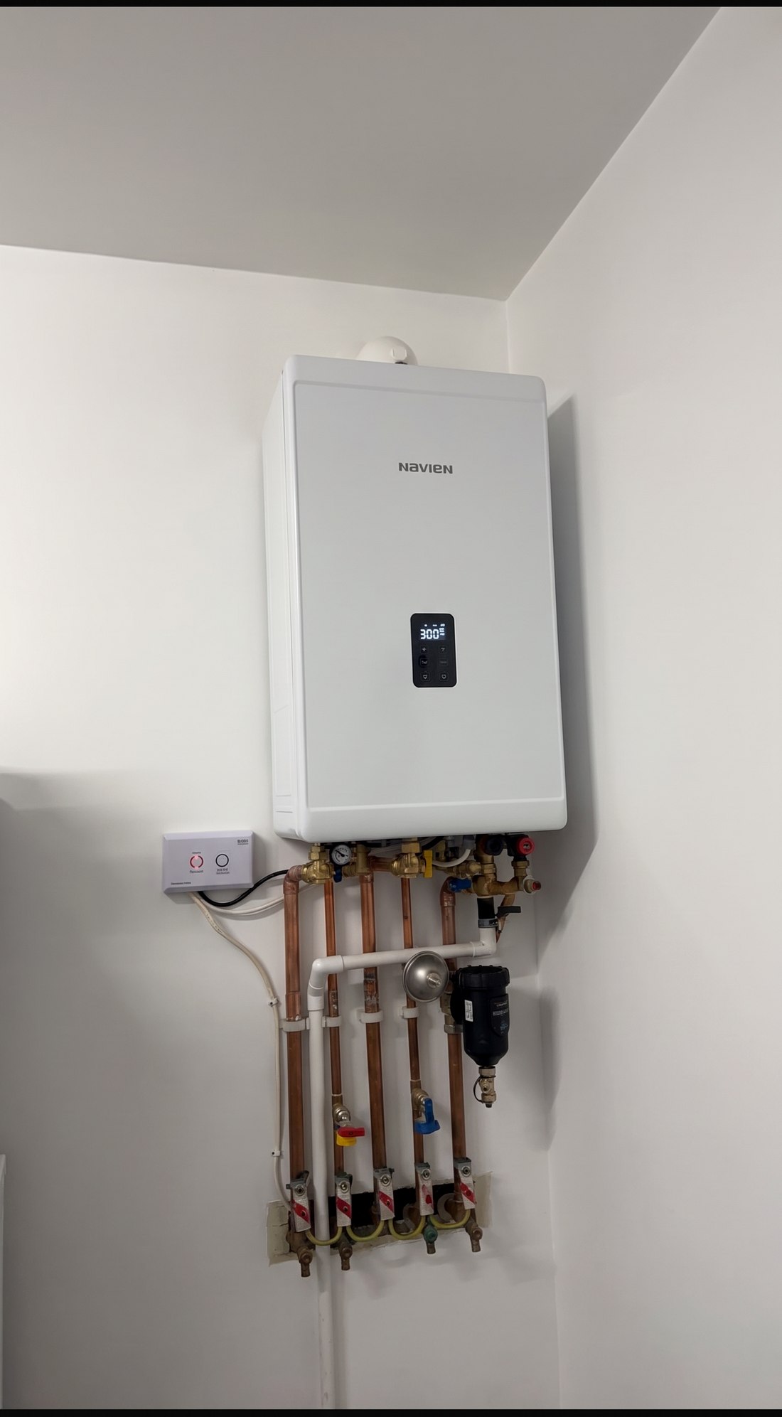 A newly installed Navien combi boiler on a kitchen wall with copper pipework, filter and isolation valves