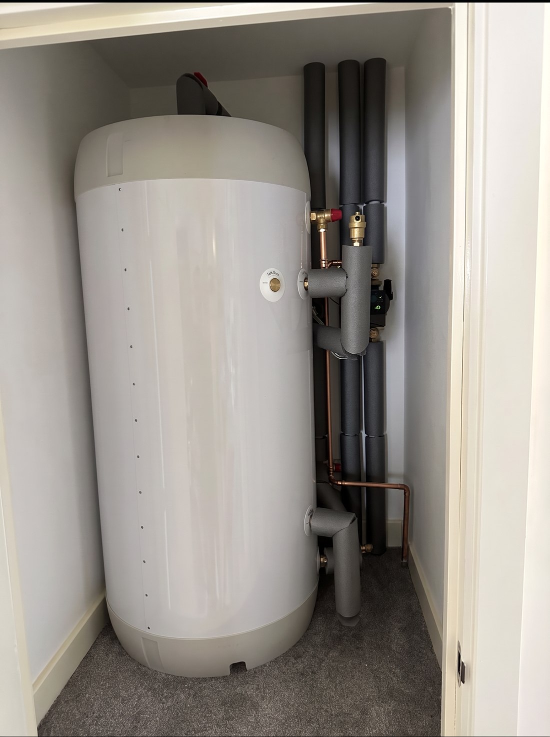 An unvented hot water cylinder fitted in a cupboard with insulated pipework and a thermostatic mixing valve